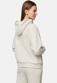 Jasno beżowy hoodie wykonany z miękkiego materiału, z dużym kapturem, luźnym krojem i ściągaczami na rękawach. Gładka tekstura i minimalistyczny design.