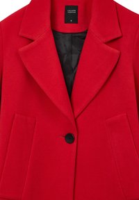 Veste en laine rouge avec revers crantés, deux poches à rabat à l'avant, une fermeture à bouton noir, et doublure noire visible.