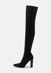 Bota negra por encima de la rodilla hecha de tejido texturizado, con punta afilada y un alto tacón cuadrado. Diseño sin costuras con detalles mínimos.