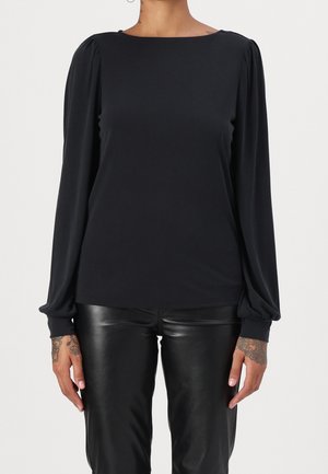 Schwarze Bluse mit langen Ärmeln und rundem Ausschnitt, mit gerafften Ärmeln und einer glatten, leichten Textur. Kombiniert mit schwarzen Lederhosen.