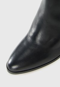 Black leather pointed-toe ankle boot with smooth texture and slight sheen on a light background.