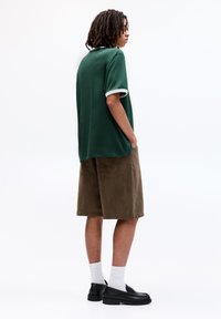 Grøn kortærmet skjorte med hvid kant, parret med brune fløjlsshorts. Sorte sko og hvide sokker fuldender speciel. 