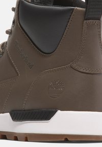 Hnědé kožené boty s černými akcenty, s prošívaným designem, vyraženým logem a bílou a hnědou podrážkou s texturovaným gripem.