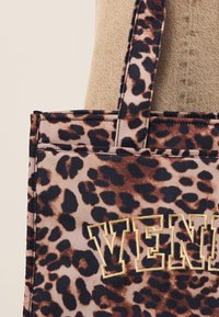 Geantă tip tote cu imprimeu leopard în nuanțe de maro și pete negre. Prezintă brodat cu aur cuvântul „VENI” pe partea din față. Material texturat, mânere rezistente.