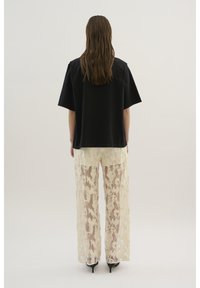 Sort oversized t-shirt med korte ærmer, parret med gennemsigtige beige blondebukser med et blomster mønster og lige snit. Sorte hæle.