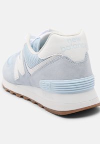 Světle modrá teniska z semišového a síťovaného materiálu. Má bílé prvky, silnou podrážku a na patě je vyraženo logo "New Balance".