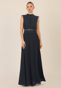 Abito maxi blu navy con bustier in pizzo, orli ondulati e vita aderente. La gonna cade delicatamente, realizzata in un tessuto morbido e leggero.