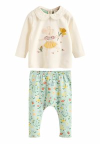 Zweiteiliges Outfit mit einem cremefarbenen Langarmtop mit Spitze am Kragen und Tierstickerei, kombiniert mit elastischen, grünen Blumenhosen.