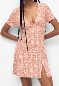 Vestido de manga corta en color naranja con un estampado floral, que cuenta con un profundo escote en V y una abertura lateral, hecho de una tela ligera para mayor comodidad.