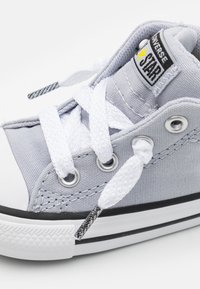 Šedé plátěné vysoké tenisky s bílými šňůrkami, gumovou špičkou, černo-bílou pruhovanou podrážkou a malou značkovou nášivkou na jazyku.