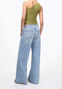 Asymmetrisk olivgrön topp i texturerat tyg, tillsammans med lös passform ljusblå denimjeans med fransar i nederkant och bakfickor.