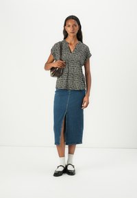 Black and white patterned short-sleeve top paired with a blue denim midi skirt featuring a front slit, worn with black shoes and white socks.