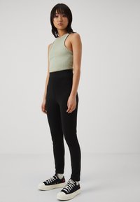 Leggings noires taille haute associés à un haut court côtelé vert clair et des baskets marines avec des semelles blanches. Design simple et ajusté.