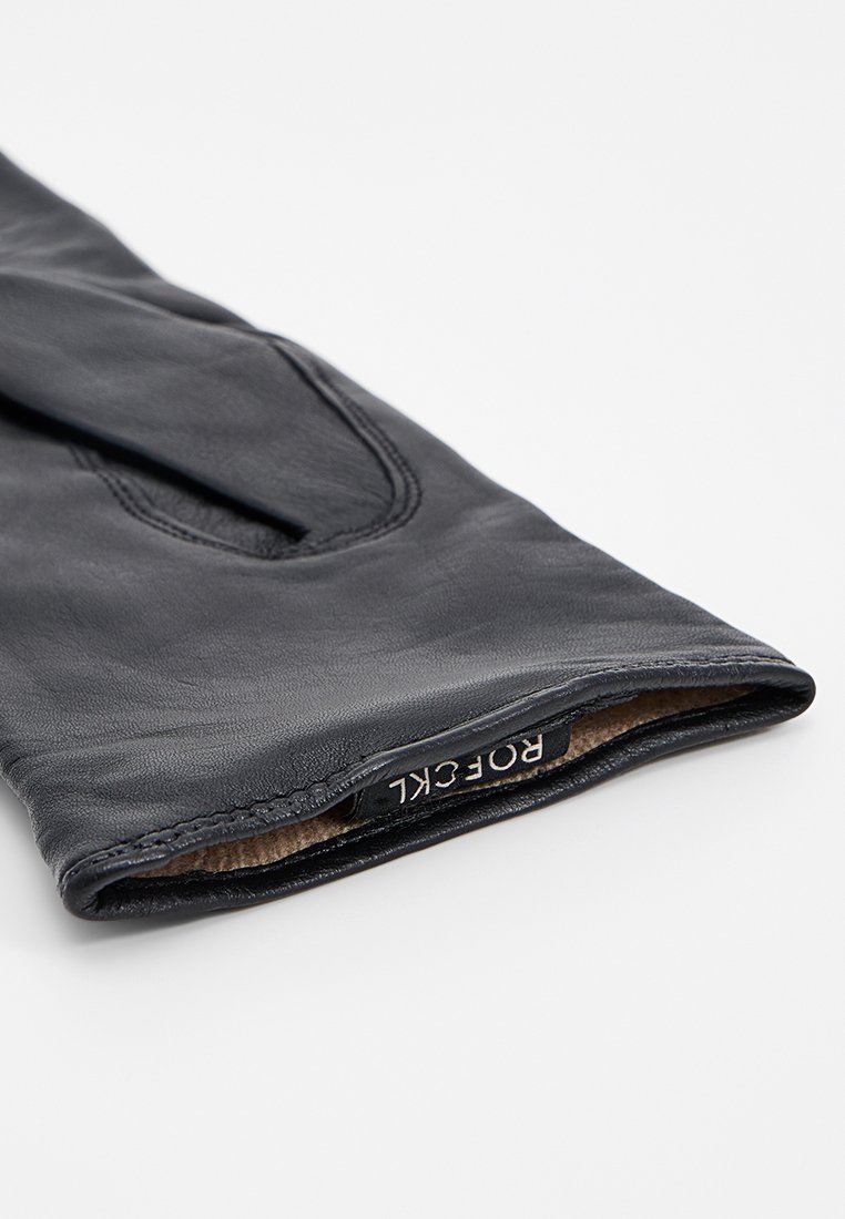 Schwarzer Lederhandschuh mit glatter Oberfläche, ausgestattet mit einem weichen Innenfutter und einem sichtbaren Markenetikett am Bündchen.