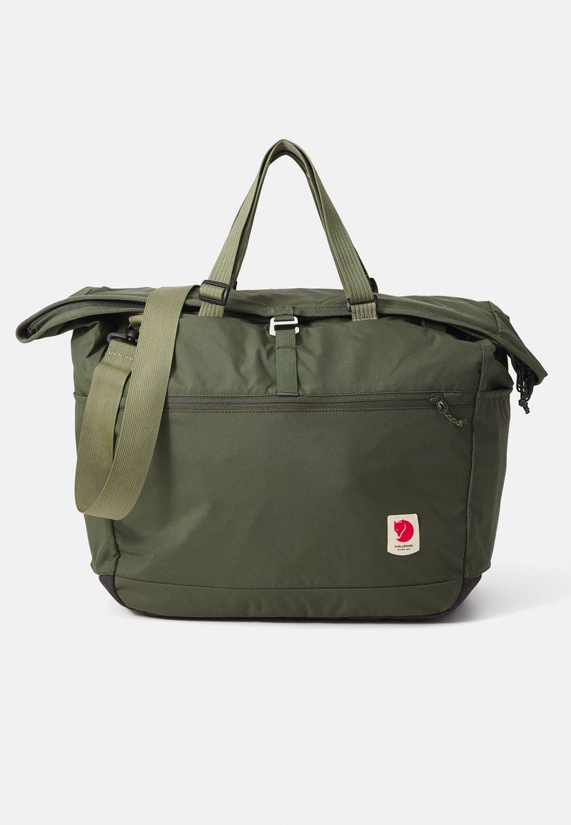 Sac fourre-tout vert olive avec double poignée et une bandoulière réglable. Il dispose d'un compartiment principal zippé et d'une poche zippée à l'avant.