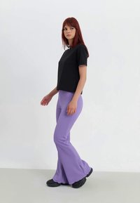 Top nero a maniche corte con design a coste, abbinato a pantaloni a palazzo lavanda. L'outfit presenta una texture liscia e una discreta cucitura bianca.