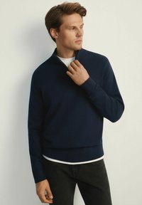 Granatowy pulower z półzamkiem, ściągaczami przy mankietach i dopasowanym krojem. Nosi się na białej koszulce z okrągłym dekoltem oraz czarnych dżinsach. Gładki materiał.