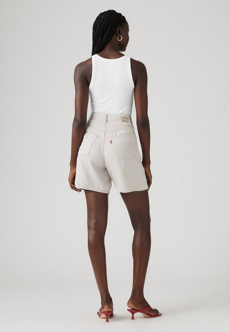 Helle graue Denim-Shorts mit hoher Taille, sichtbaren Nähten und Gesäßtaschen. Kombiniert mit einem weißen Tanktop und roten Sandalen mit Absatz.