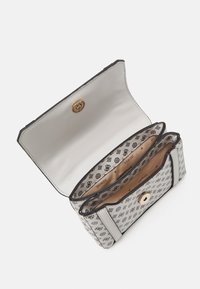 Borsa sintetica bianca con un motivo logo nero, hardware dorato e interno beige. Presenta due scomparti e una chiusura a scatto.