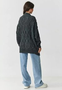 Gruby, ciemnoszary sweter z dzianiny o teksturowanym wzorze w diamenty, luźny krój i ściągacze, w połączeniu z niebieskimi spodniami o szerokich nogawkach.