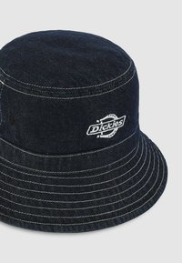 Cappello a secchiello in denim blu scuro con cuciture bianche e logo circolare "Dickies". Presenta un design morbido e strutturato e una visiera larga.