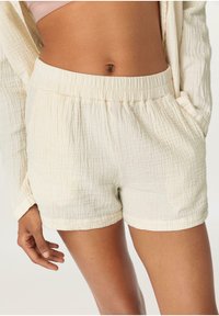 Ljusbeiga shorts i texturerad bomull med elastisk midja och sidofickor. Tyget har en mjuk, rynkad yta.