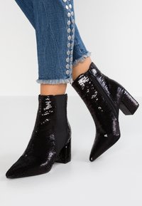 Stivaletti neri con paillettes, punta affusolata, tacco a blocco e zip laterale. Il design presenta una combinazione di texture lucide e opache.