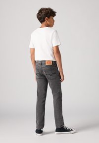 Vaqueros grises con corte recto, parche de cuero en la parte trasera y dos bolsillos traseros. Combinados con una camiseta blanca de manga corta y zapatillas.