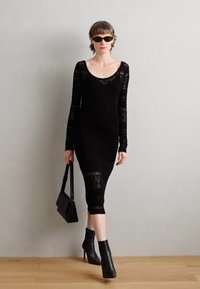 Abito lungo nero a maniche lunghe con silhouette aderente e scollo rotondo. Abbinato a stivaletti neri alla caviglia e una piccola borsa a tracollo.