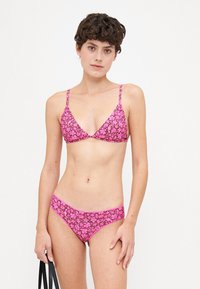 Rózsaszín virágmintás bikini szett, amely tartalmaz egy háromszög alakú bralette-t vékony pántokkal és egy hozzá illő bikini alsót, mindkettő virágminták keverékével.