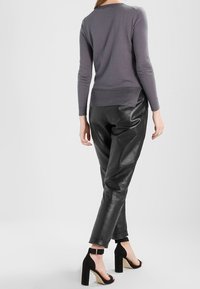 Grå långärmad topp med rund halsringning, ihop med svarta läderbyxor och svarta klackskor med ankelsnöre. Släta texturer och figurnära design.
