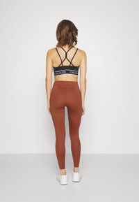 Soutien-gorge de sport noir avec un design dos strappy, leggings marron taille haute et chaussures de sport blanches, vues de dos sur un fond neutre.