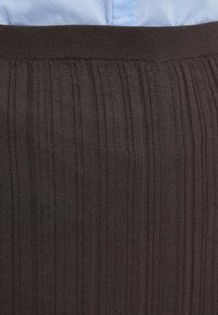 Tissu en maille côtelée brun foncé avec une apparence texturée et une ceinture élastique, couvrant partiellement une chemise bleu clair en dessous.