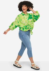 Maglietta verde tie-dye con bottoni davanti, annodata in vita; abbinata a jeans fitted azzurri e sandali bianchi.