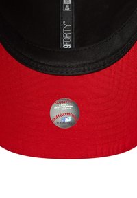 Rote Baseballkappe mit schwarzem Innenrand, versehen mit einem runden MLB-Aufkleber auf dem Schirm. Das Material wirkt glatt mit strukturiertem Design.