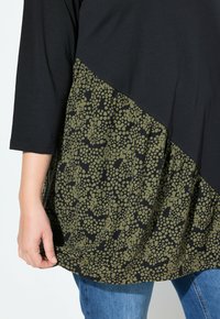 Top nero con maniche a tre quarti, caratterizzato da una parte inferiore in verde oliva arricciata con un motivo a pois, abbinato a jeans blu.