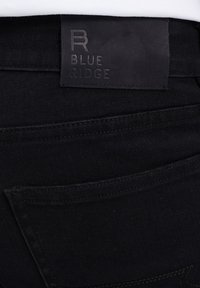 Černé džíny z denimu s hladkou texturou a zadní kapsou, s tmavým obdélníkovým štítkem vyraženým nápisem "B BLUE RIDGE."