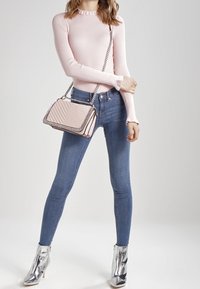 Top a maniche lunghe rosa a coste, jeans blu a vita alta e una borsa a tracolla rosa chiaro trapuntata con tracolla a catena, abbinata a stivaletti argentati.