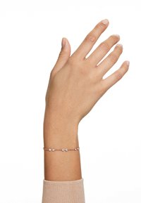 Un primer plano de una mano que lleva una delicada pulsera con pequeñas piedras brillantes, contra un fondo blanco liso.
