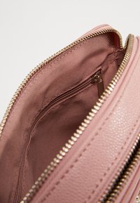 Interno di borsa in pelle rosa con una texture liscia, cerniera in metallo dorato e una tasca interna aggiuntiva con chiusura a zip.
