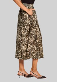 Vrouw in een midi-jurk met luipaardprint en een elastische tailleband, met zwarte kittenheel slingback schoenen, hand in de zak.