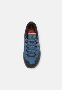 Niebiesko-czarny but sportowy z teksturowaną siateczką, pomarańczowymi akcentami i czarną gumową podeszwą. Posiada współgrające sznurowadła i logo marki.