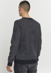 Marineblå strikket trøje med et struktureret mønster, ribbede manchetter og nederkant samt rund hals. Stoffet ser blødt og medium tungt ud.