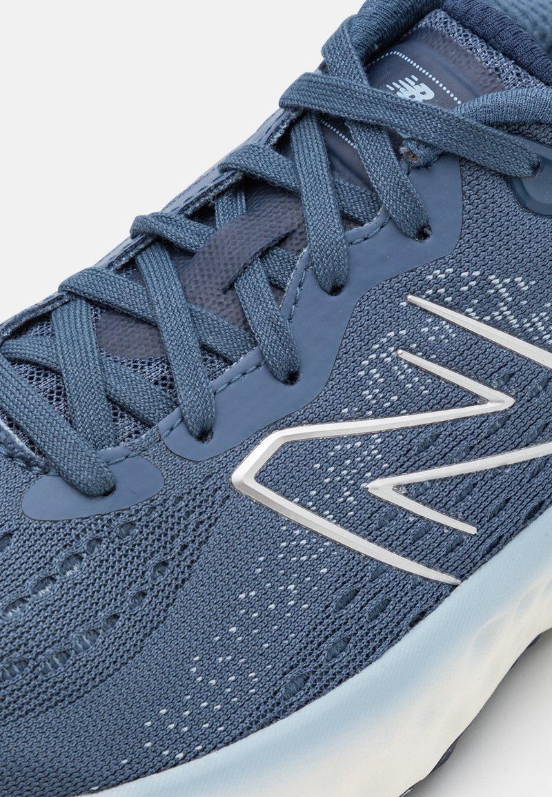 Zapatilla deportiva azul con parte superior de malla texturizada, cordones tonales y un acento de logo plateado en el costado, con una suela blanca acolchada.
