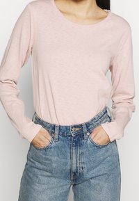 Ljusrosa långärmad skjorta med rund halsringning, kombinerad med högmidjade blå denimjeans med knapp- och dragkedjeslutning.