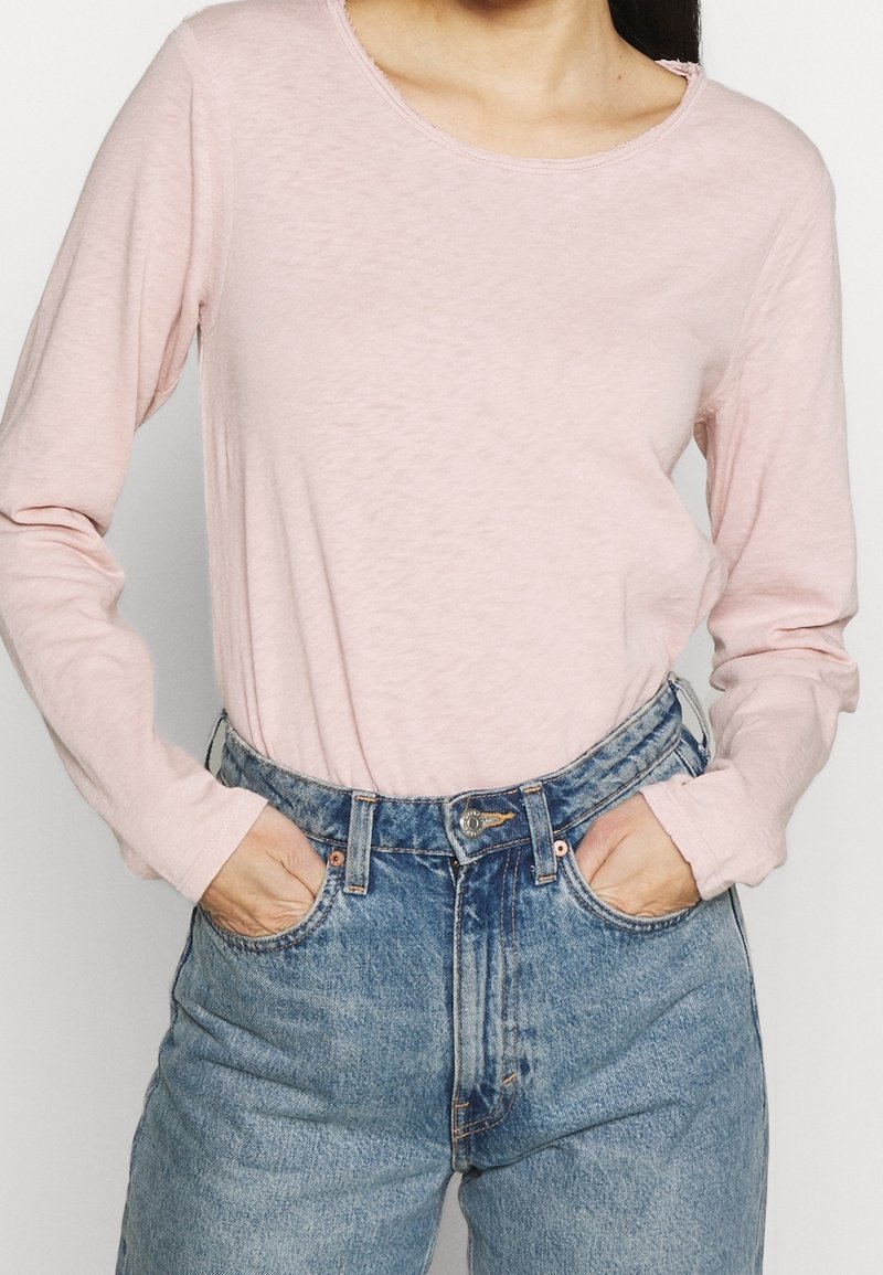 Ljusrosa långärmad skjorta med rund halsringning, kombinerad med högmidjade blå denimjeans med knapp- och dragkedjeslutning.