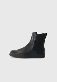 Botas de tobillo de cuero negro con una superficie texturizada, paneles laterales elásticos y una suela de goma negra sólida. Diseñadas para facilitar el calce.