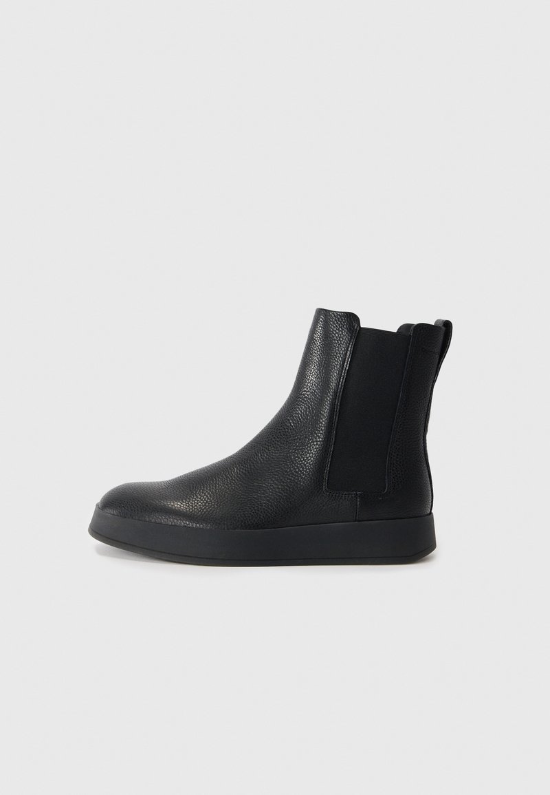 Botas de tobillo de cuero negro con una superficie texturizada, paneles laterales elásticos y una suela de goma negra sólida. Diseñadas para facilitar el calce.