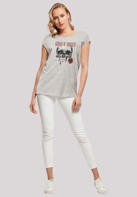 Lichtgrijs T-shirt met een zwarte schedelafbeelding en een rode roos, gecombineerd met witte skinny jeans en witte sneakers.