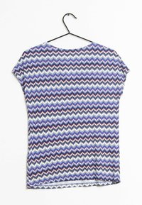 Top a maniche corte con motivo a zigzag in blu, rosso e bianco. Tessuto morbido con colletto rotondo, presentato su una gruccia nera su sfondo bianco.